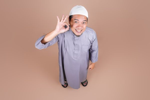 High Angle of Young Asian Muslim Man Showing OK Sign Isolated on Beige Background High Angle of Young Asian Muslim Man Showing OK Sign Isolated on Beige Background